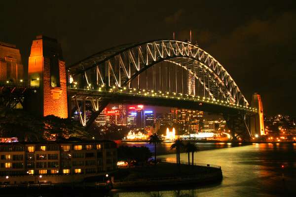The iconic Sydney Harbour Bridge illuminated at night, with its majestic arch spanning the harbour against a backdrop of city lights. Tales of ghostly encounters on this landmark add an eerie twist to the Sydney ghost tours experience.