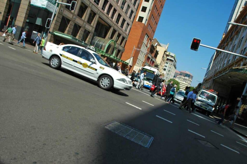 Busy city intersection in Sydney with taxis and pedestrians, showcasing typical traffic and transportation options, relevant to discussing the availability and comparison of Ubers in Sydney