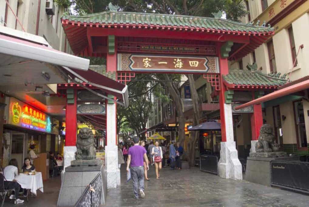 Pedestrians walking through the ornate Paifang at the entrance of Chinatown in Sydney, symbolising the city's multicultural fabric and diverse communities as one of the pros of living in Sydney.