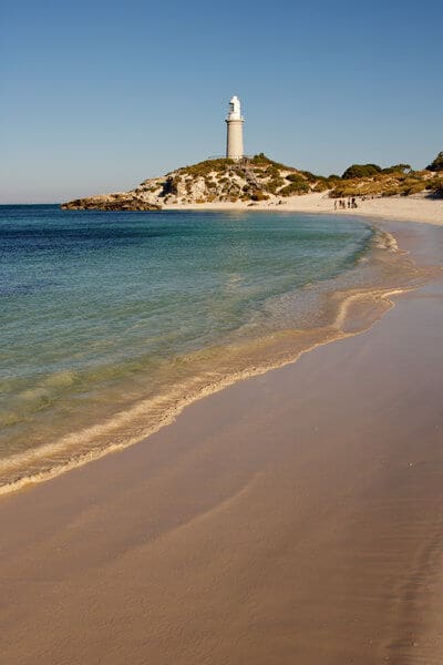 Rottnest Island's picturesque lighthouse stands as a serene beacon above the tranquil beach, a romantic spot for a Valentine's Day getaway near Perth, with crystal-clear waters gently lapping the sandy shore.