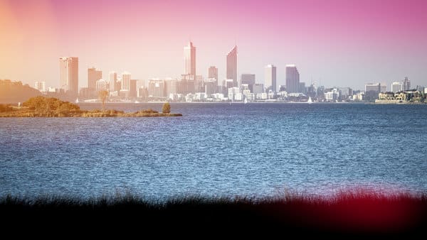 The Perth skyline against a gradient pink and blue sky, viewed from across the water, capturing the essence of the city at dusk. The image depicts the natural beauty encountered when travelling and is relevant to the discussion on adjusting to the time difference when visiting different cities in Australia, such as Sydney and Perth.