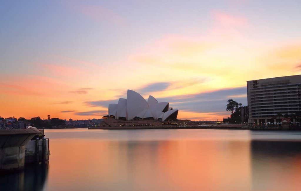 Sydney Opera House at sunset, reflecting on the calm waters, a serene view often enjoyed on walking tours in Sydney.