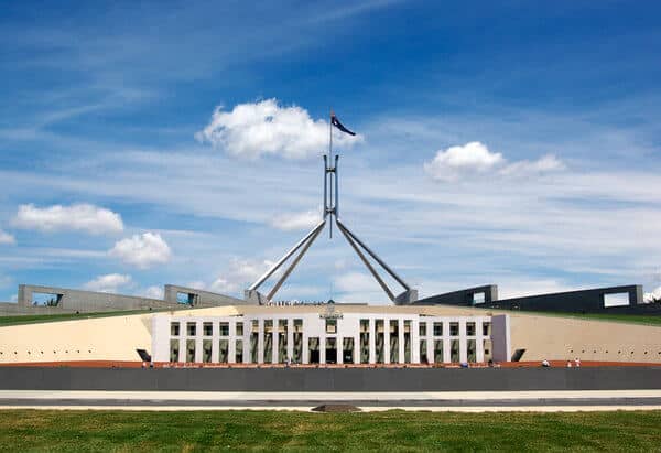 The iconic Parliament House in Canberra, with its high flagpole and striking facade against a blue sky, captures the essence of Australian democracy. An essential highlight for 'Canberra tours from Sydney' blog post, symbolising the political heart of Australia.