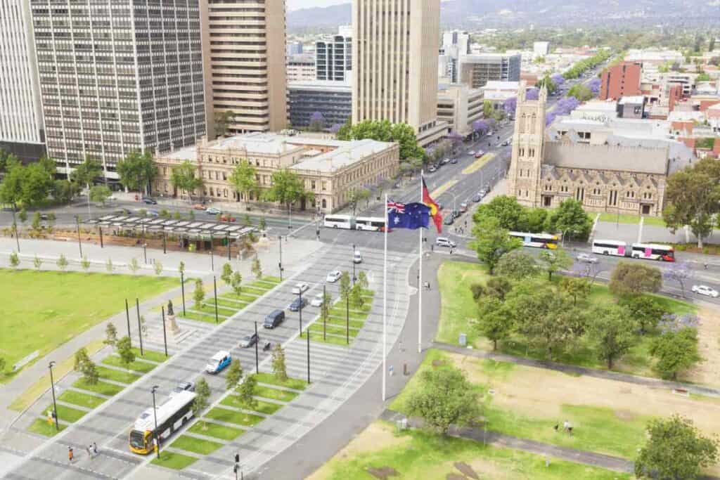 Aerial view of Adelaide's city centre during the daytime, showcasing its streets, historic buildings, and modern structures. This image highlights the destination of Adelaide from Sydney, often travelled to by road or air, offering a glimpse of the city's urban environment.