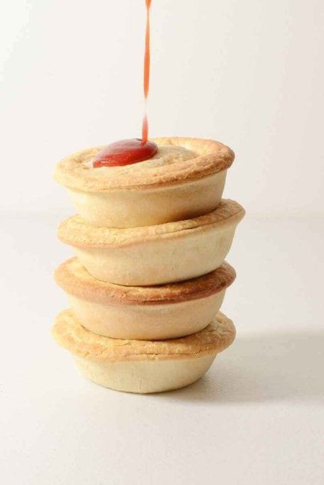Stack of traditional Australian meat pies with tomato sauce being poured on top, a classic example of the local delicacies encountered on Sydney food tours.