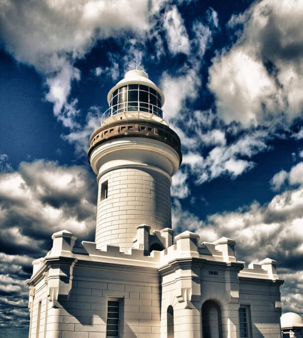 Historic Byron Bay Lighthouse standing tall against a dramatic cloudy sky, highlighting a must-see location in many Australia travel deals.