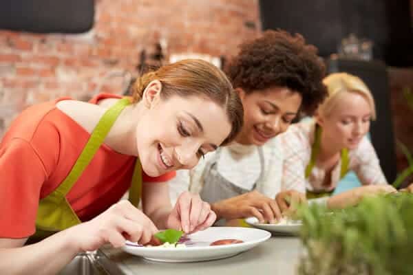 Smiling women engaging in a cooking class, meticulously garnishing dishes, which is one of the cozy indoor activities to enjoy in Adelaide during winter.