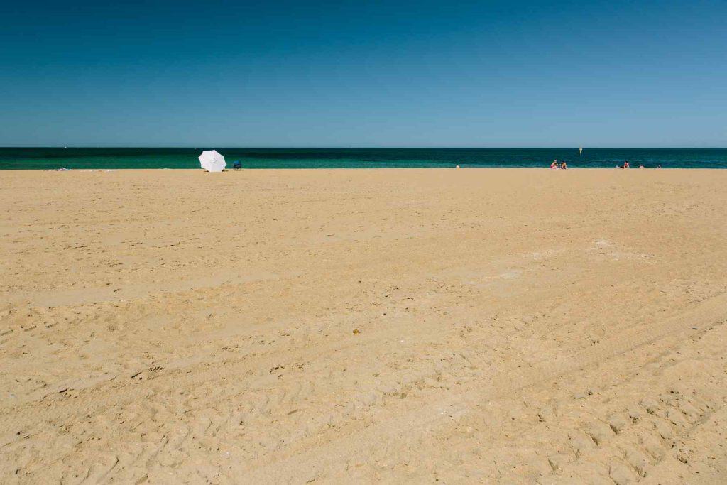 Mordialloc Beach in Melbourne. A large white umbrella near the waterline shelters its occupants.