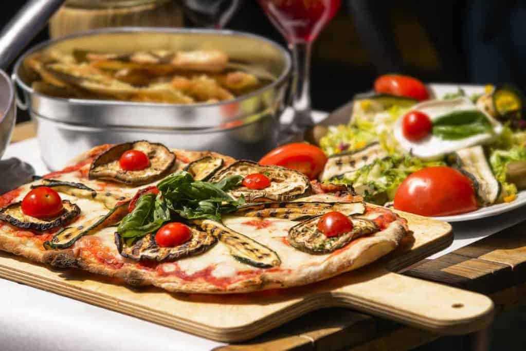 A rustic Italian feast featuring a grilled vegetable pizza on a wooden paddle, a fresh salad, and a pot of steaming pasta, reminiscent of the delicious meals sampled on gourmet food tours in Sydney.