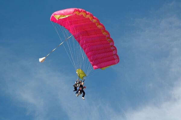 A couple enjoying a tandem skydive on Valentine's Day in Perth, gliding through the blue sky with a vivid pink parachute, symbolizing romance and adventure.