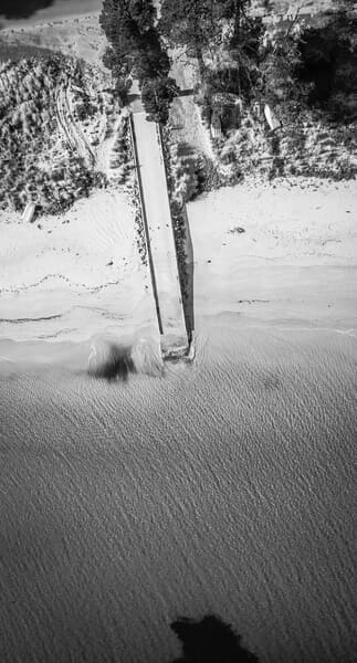 Black and white aerial photograph of the textured sands of Dennes Point Beach on Bruny Island, with a lone wooden structure casting a stark shadow, highlighting the island's unique charm and prompting visitors to ask, 'Is Bruny Island worth visiting?