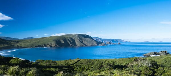 A panoramic view of Bruny Island's coastline, with its pristine beaches and lush greenery, under the clear blue sky, perfect for a secluded Valentine's Day escape near Hobart.