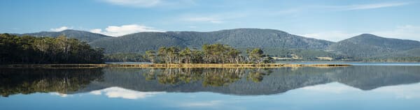 Mirror-like reflections on the calm waters at a tranquil lagoon on Bruny Island, with a backdrop of lush hills, exemplifying the peaceful and pristine environments that make the island an enchanting place to visit.