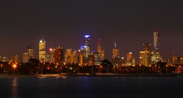 The Melbourne skyline at night, with its array of brightly lit buildings and tranquil water reflections, invites consideration of the city's time zone in relation to Sydney's, pertinent to the query if Melbourne and Sydney share the same time zone.