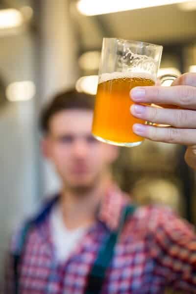 A brewer examining a glass of pale ale, with a focus on the beer's clarity and color, during a quality check at a brewery tour in Brisbane, reflecting the meticulous craft behind brewing.