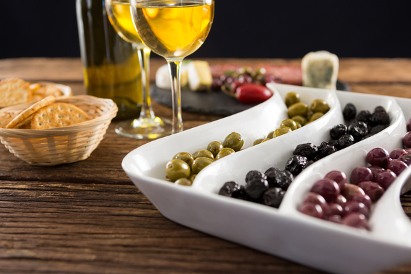 Close up of marinated olives with bottle of wine and food