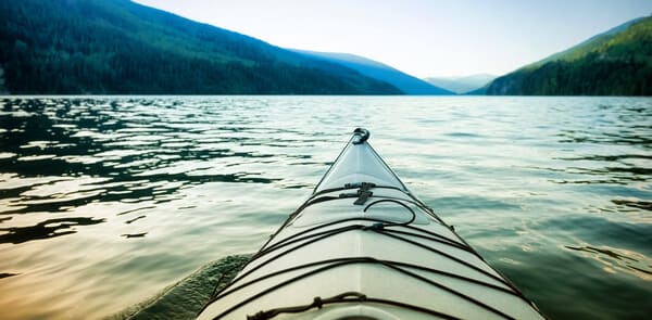 The bow of a kayak cutting through the tranquil waters of a lake, flanked by forested hills, offering an adventurous yet intimate experience for Valentine's Day in Hobart.