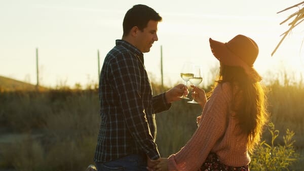 A couple holding hands and toasting with glasses of white wine in the golden light of sunset, enjoying a premium wine tour on Valentine's Day in Hobart, Tasmania.