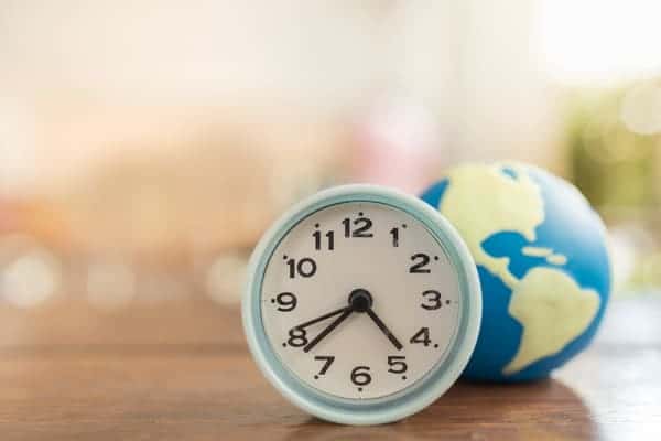 Analog clock in the foreground with a blurred small globe in the background, symbolising global time coordination. This image supports the blog post's theme on managing the time difference between Sydney and Perth for international travellers.