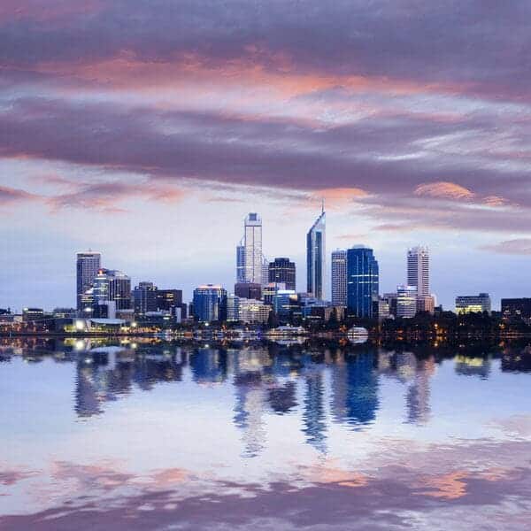 Perth's cityscape reflects romantically on the Swan River at dusk, with soft pink and purple hues in the sky, a serene setting for a Valentine's Day evening stroll or cruise in Perth, Australia