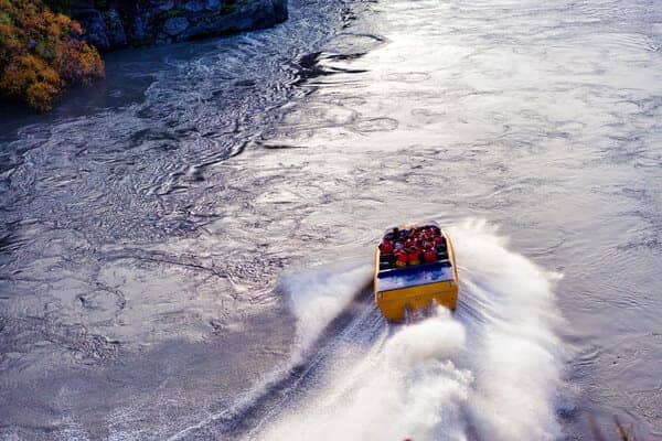 Thrill-seekers enjoy a high-speed jet boat ride on a swirling river, reminiscent of the excitement of bungee jumping near the Sydney Harbour Bridge.