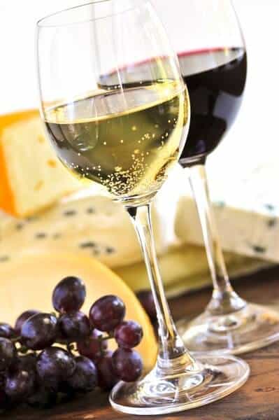 A close-up of two wine glasses, one with white wine and the other with red, alongside a selection of cheese and grapes, representing the indulgent experiences on offer with wine tours in Hobart.
