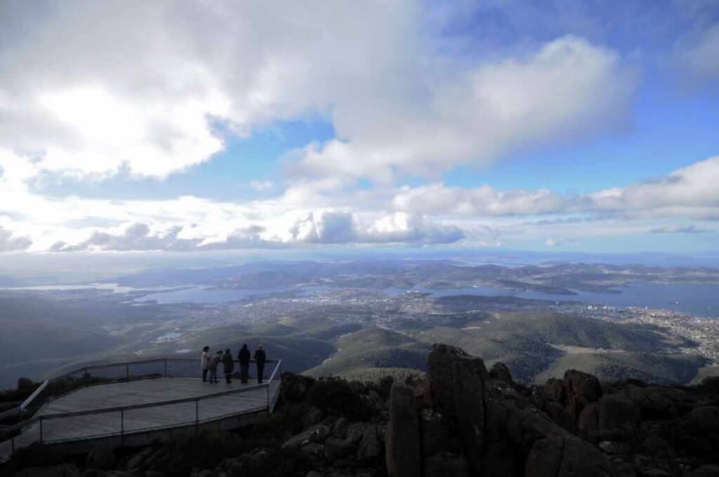Visitors at the summit lookout on Mount Wellington overlooking the panoramic view of Hobart, Tasmania, under a dramatic winter sky. A must-visit for travellers searching for unique things to do in Hobart in winter.