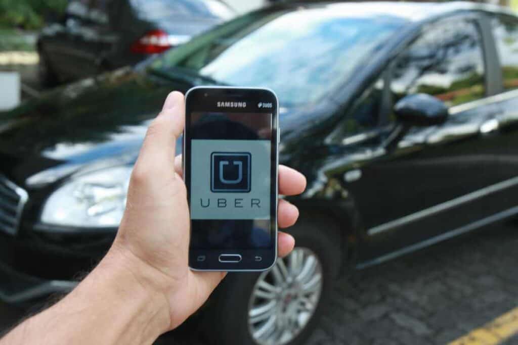 Hand holding a smartphone displaying the Uber app in front of a black car, illustrating the ease of booking an Uber in Sydney through mobile technology.