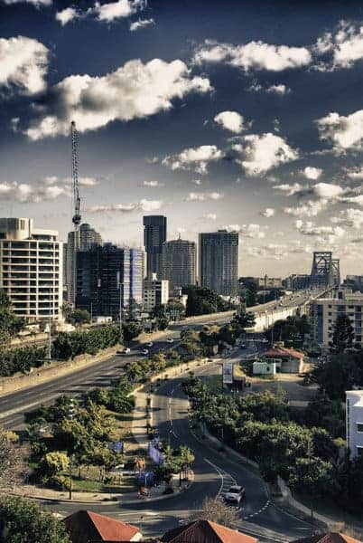 Dynamic clouds hover above the urban skyline of Brisbane, with a view of the iconic Story Bridge, encapsulating the city’s energetic pace which is often contrasted with the laid-back atmosphere of Adelaide in discussions about Brisbane and Adelaide.