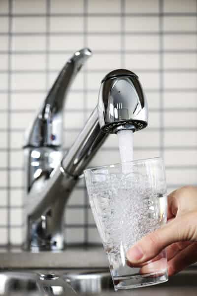 A hand filling a clear glass with tap water from a modern kitchen faucet, questioning the potability of tap water while travelling in Bali.