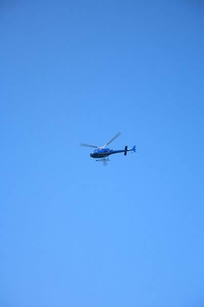 A blue helicopter flying against a clear blue sky, providing aerial tours that offer an alternative to bungee jumping on the Sydney Harbour Bridge.