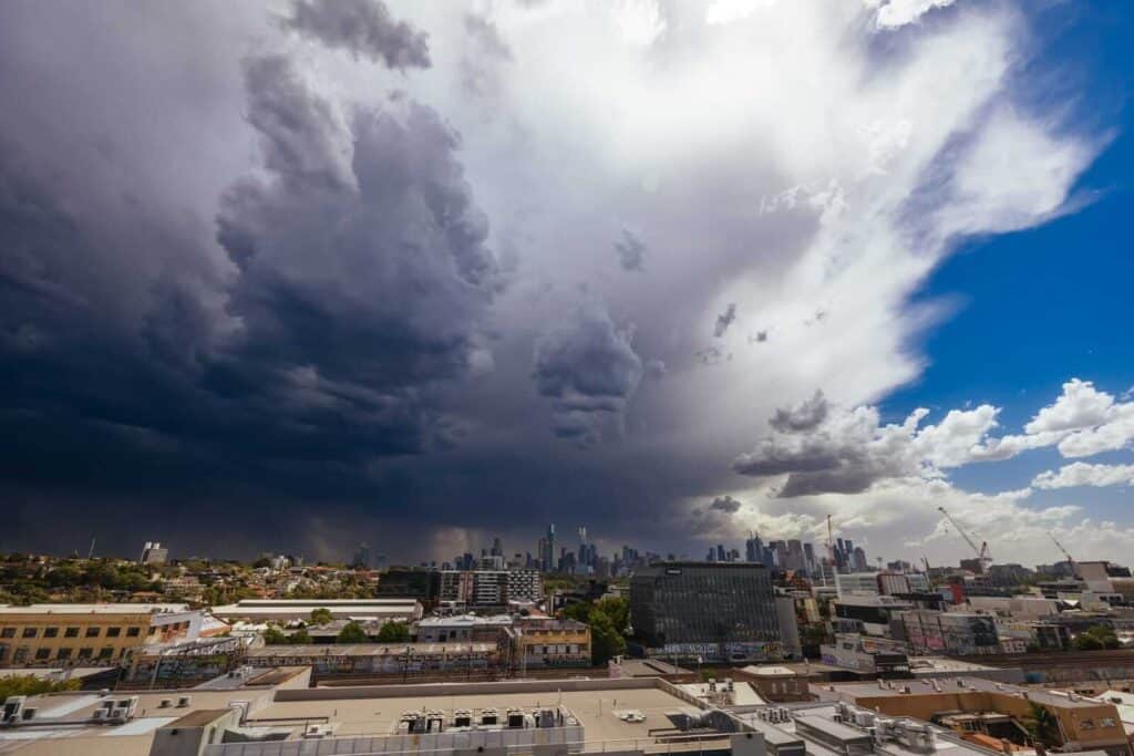 A dramatic contrast of a brewing summer storm over Melbourne, with dark thunderclouds on one side and clear skies on the other, over the city's skyline. This striking image highlights the erratic nature of Melbourne's climate, underscoring the blog's topic of 'why Melbourne weather is unpredictable'.