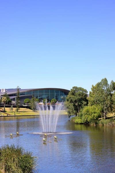 A serene fountain dances in the River Torrens with the Adelaide Convention Centre in the background, illustrating Adelaide’s blend of natural beauty and modern facilities, a comparison point in the Brisbane vs. Adelaide debate.