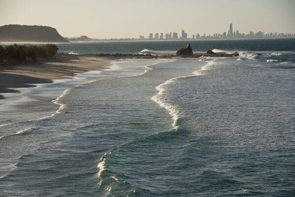 Serene Gold Coast beach in the early morning, December, illustrating the ideal setting for deciding what to wear in Gold Coast in December, with gentle waves and a clear sky.