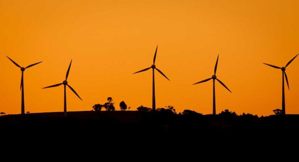Silhouette of wind turbines against a vibrant orange sky at dusk.
