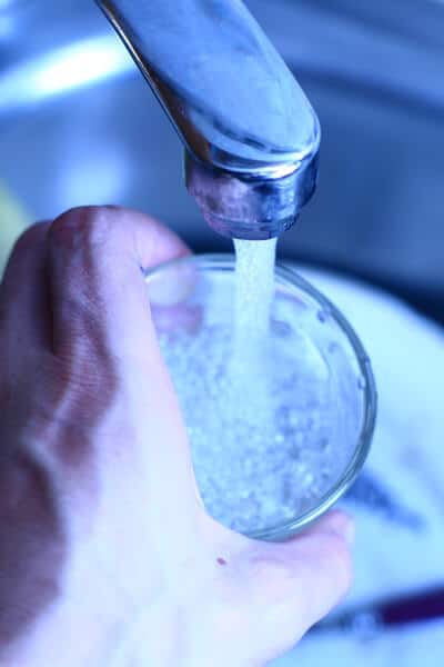 Hand holding a glass under a running tap, illustrating the query 'can you drink tap water in Bali?' and the importance of knowing water safety abroad.