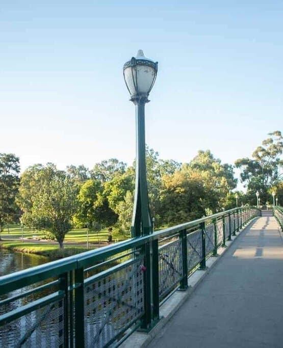 A pedestrian bridge over the River Torrens in Adelaide's Botanic Gardens, bathed in sunshine with verdant trees along the banks, indicating the mild weather conditions and answering the query, 'Does snow ever fall in Adelaide?'