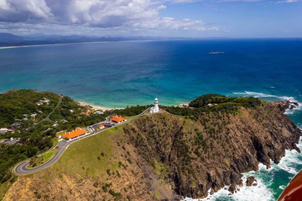 Aerial view of Cape Byron Lighthouse perched on the coastline above turquoise waters, one of the most iconic sights on any Byron Bay bucket list of must-do activities.
