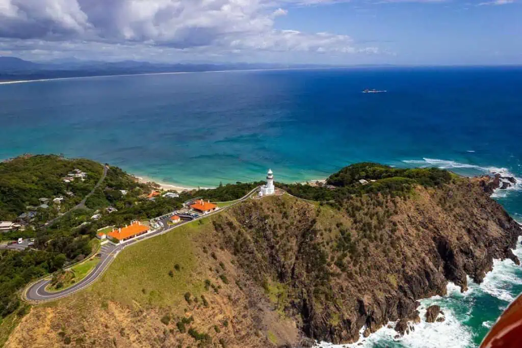 An aerial view of Cape Byron Lighthouse perched on a rocky headland overlooking the turquoise waters and beaches of Byron Bay. This image highlights the lighthouse’s iconic location and its stunning coastal surroundings, which are key features in the blog post about exploring Cape Byron.