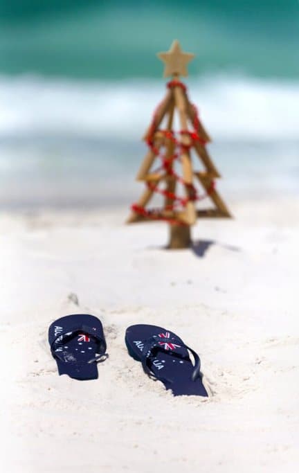 Australian flag thongs in the sand near a small Christmas tree on a sunny beach. This image showcases a unique Australian Christmas tradition, highlighting the contrast between the warm summer holiday and the festive spirit. Fun facts about Christmas in Australia often include celebrating with beach trips and outdoor activities due to the warm weather.