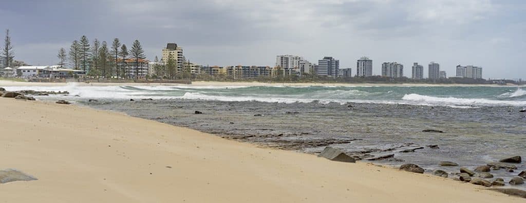 Overcast day along a quiet beach on the Sunshine Coast with high-rise buildings in the distance, capturing the balance between natural coastal beauty and urban development that reflects the benefits and drawbacks of living on the Sunshine Coast.
