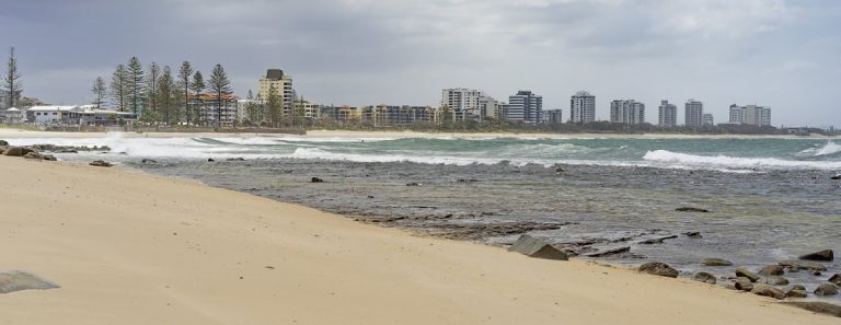 Overcast day along a quiet beach on the Sunshine Coast with high-rise buildings in the distance, capturing the balance between natural coastal beauty and urban development that reflects the benefits and drawbacks of living on the Sunshine Coast.