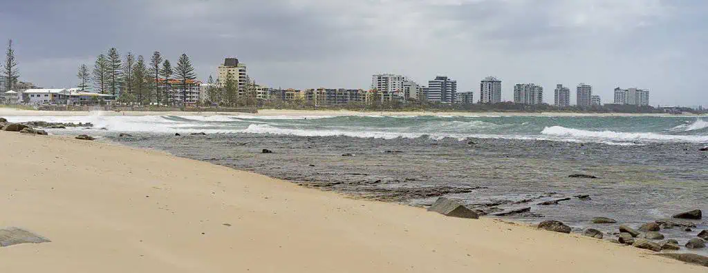 Overcast day along a quiet beach on the Sunshine Coast with high-rise buildings in the distance, capturing the balance between natural coastal beauty and urban development that reflects the benefits and drawbacks of living on the Sunshine Coast.