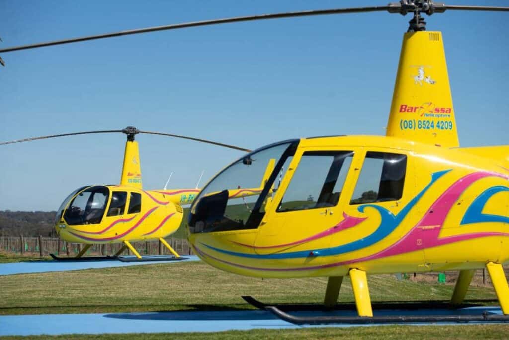 Two vibrant yellow Robinson R44 helicopters parked side by side on a helipad, ready for takeoff in the Barossa Valley. This image illustrates the excitement of helicopter joy flights Adelaide, providing a glimpse into the thrilling aerial adventures available for exploring South Australia's scenic landscapes.