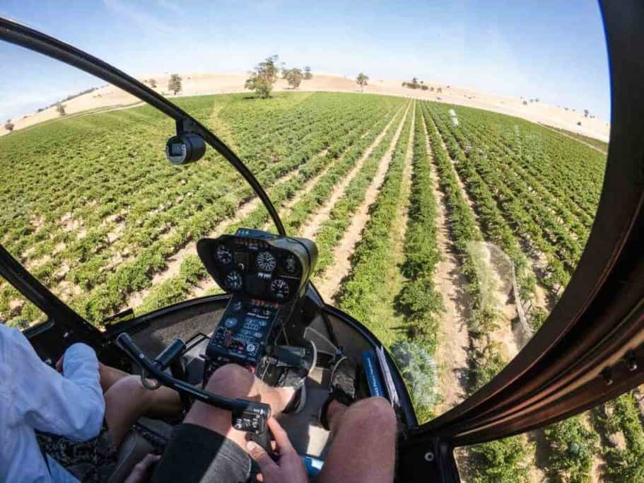 View from inside a helicopter cockpit, overlooking lush vineyards in the Barossa Valley. The helicopter’s instruments and the pilot's hands on the controls are visible, capturing the essence of flights to the Barossa Valley and the unique perspective it offers of the region's famous wine-producing landscapes.