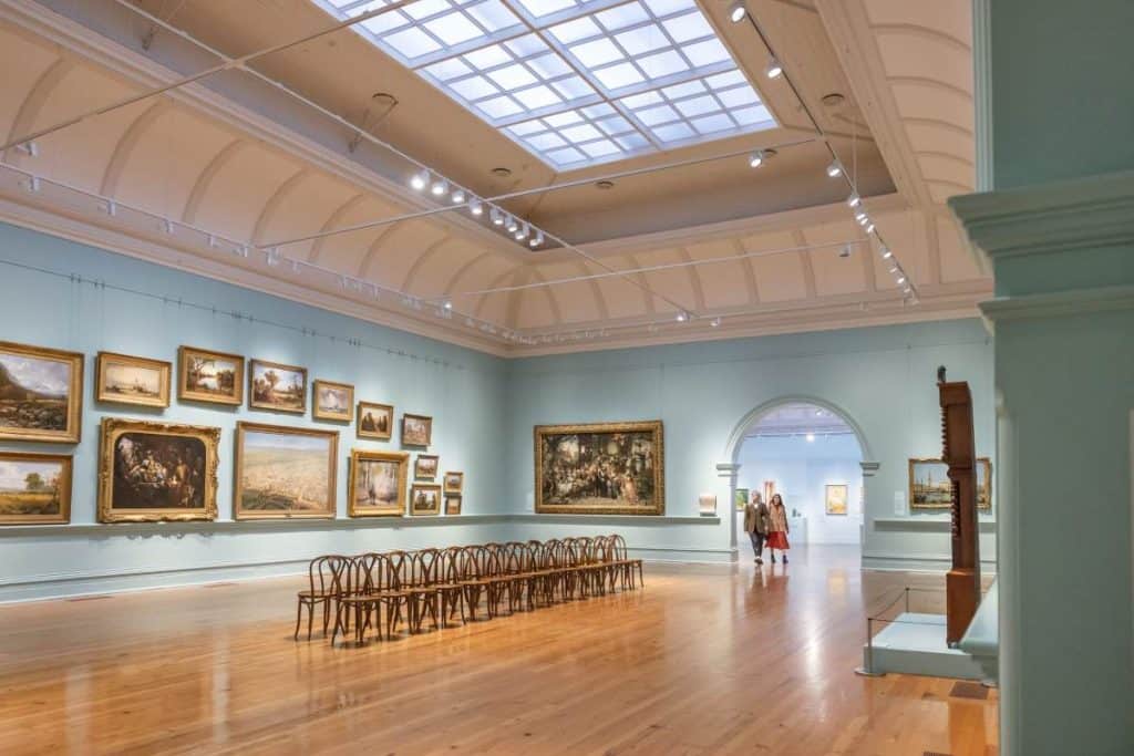 An interior view of the Bendigo Art Gallery, featuring classic paintings in ornate gold frames and a high-arched ceiling with skylights. The gallery is a key cultural attraction, reflecting the rich arts scene that adds to the lifestyle appeal discussed in the blog post about the advantages and disadvantages of living in Bendigo.