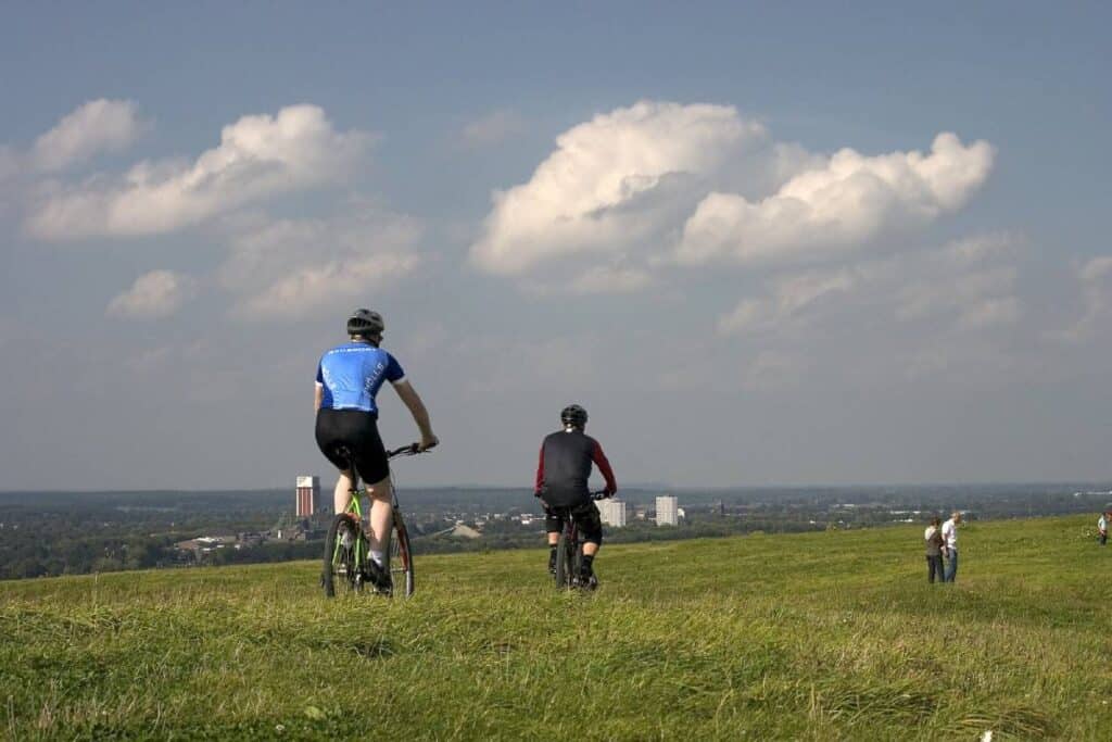 Two cyclists riding on a grassy hill with a view of a city skyline in the distance. This image highlights an outdoor biking tour experience.
