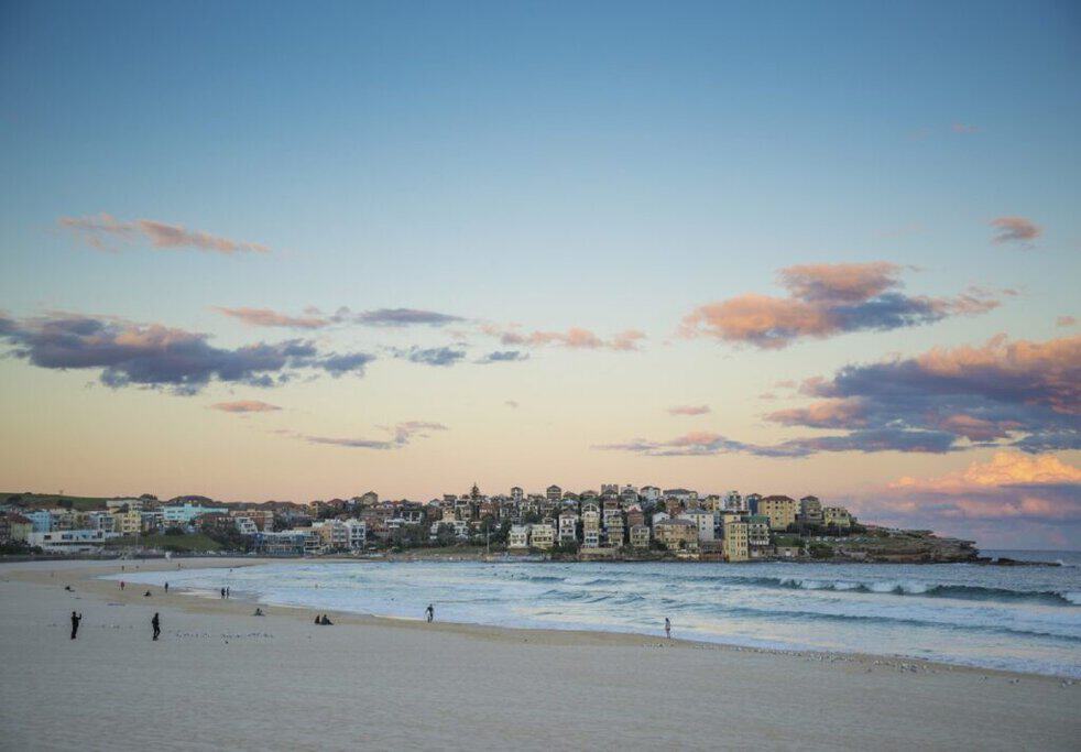 Sunset over Bondi Beach in Sydney, Australia, with soft orange and pink hues in the sky, reflecting off the waves. The image highlights one of the best spots to view Australian sunsets, complementing the blog post about must-see sunset locations across Australia.