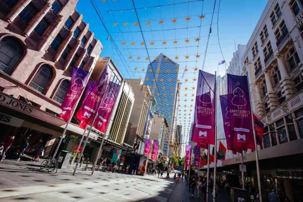Christmas decorations hanging above Bourke Street Mall in Melbourne, with festive banners and stars lighting up the city. This scene highlights one of the best Melbourne Christmas events, showcasing the vibrant holiday atmosphere in the city's shopping district.