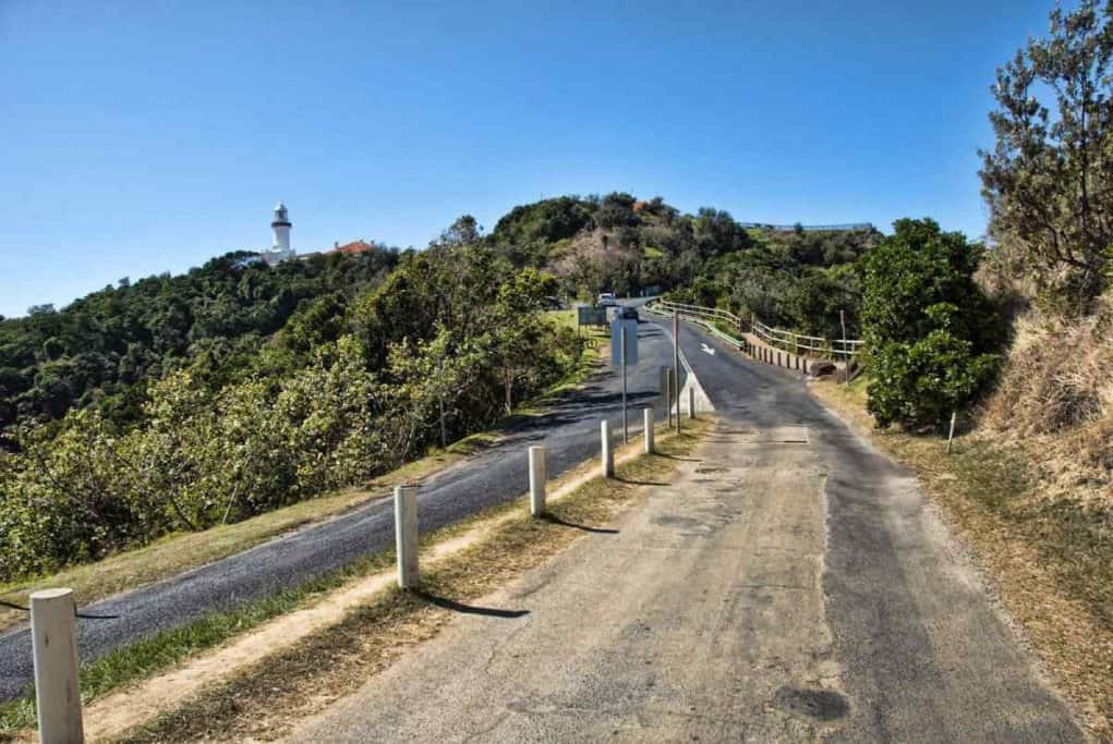 View of the path leading to Cape Byron Lighthouse, surrounded by lush greenery under a clear blue sky. This image illustrates the scenic approach to the lighthouse, highlighting the natural beauty and accessibility of this iconic destination.